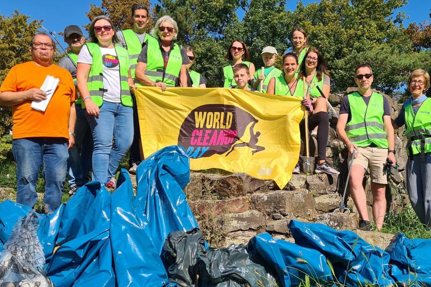 Gruppenbild, Personen mit Warnwesten und Müllzangen halten ein Banner des World Cleanup Days, im Vordergrund Müllsäcke